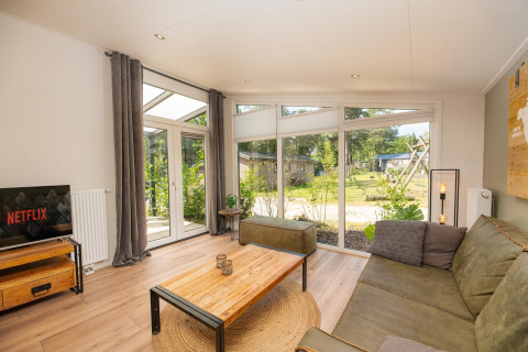 Soggiorno della Forest Lodge al Veluwepark de Bosgraaf, Paesi Bassi, con grandi finestre e arredi moderni.