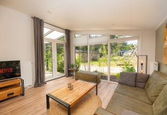 Stue i Forest Lodge ved Veluwepark de Bosgraaf, Nederlandene, med store vinduer og moderne indretning.