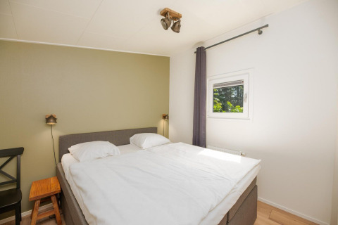 Dormitorio en Forest Lodge en Veluwepark de Bosgraaf, Países Bajos, con cama doble y ventana pequeña.