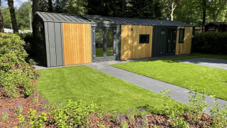 Moderne trælodge med store vinduer og velplejet have ved Cozy Chalet i Veluwepark de Bosgraaf, Holland.