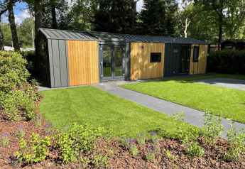 Moderne trælodge med store vinduer og velplejet have ved Cozy Chalet i Veluwepark de Bosgraaf, Holland.