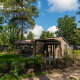 Moderne Loevestein-lodge i grøn skov, med terrasse, havemøbler og parasol under blå himmel.