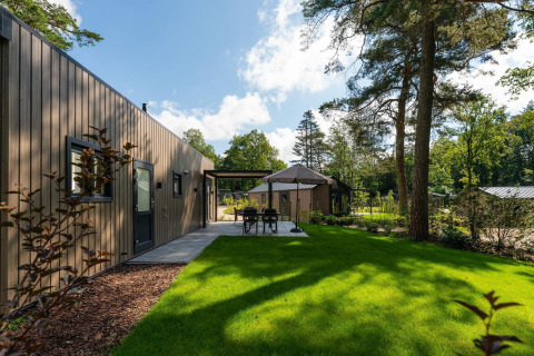 Eine moderne Lodge mit Terrasse, Sitzbereich und großer Rasenfläche, umgeben von Wald und Bäumen.