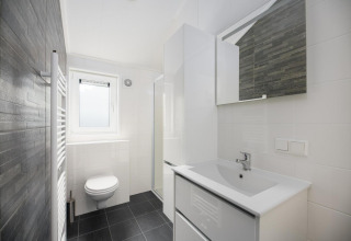 Modernes, helles Badezimmer in der Loevestein-Lodge im Veluwepark de Bosgraaf, Niederlande, mit weißen und grauen Fliesen.