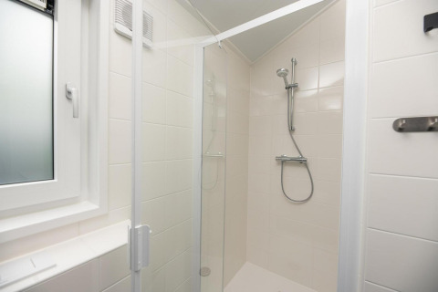 Moderna cabina de ducha con puerta de cristal y paredes de azulejos blancos en Loevestein, Veluwepark de Bosgraaf, Países Bajos.