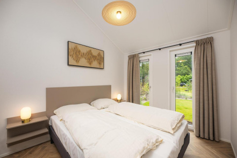 Dormitorio en la cabaña Loevestein del Veluwepark de Bosgraaf, Países Bajos, cama doble y vista al jardín.