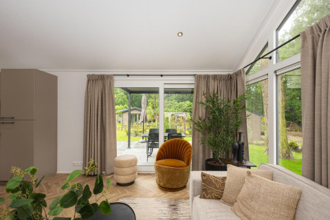 Sala de estar luminosa y moderna en la Lodge Loevestein, Veluwepark de Bosgraaf, Países Bajos, con vista al jardín.