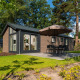 En moderne Velthorst-lodge med stort vindue, terrasse, bord, stole og solparasol omgivet af natur.