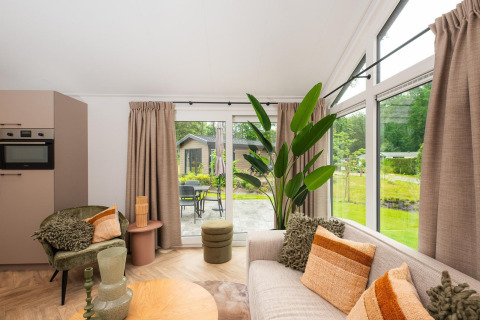 Helle Lodge im Veluwepark de Bosgraaf, Niederlande, mit gemütlicher Sitzecke, Pflanzen und großem Fenster.