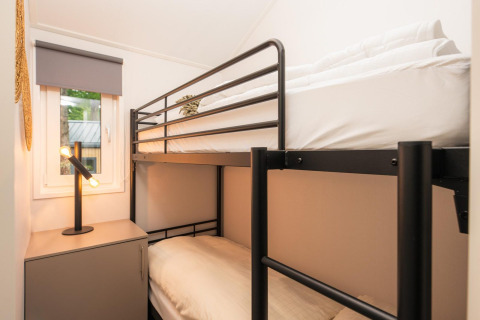 Litera moderna y mesita de noche con lámpara en una habitación de Velthorst, Veluwepark de Bosgraaf, Países Bajos.