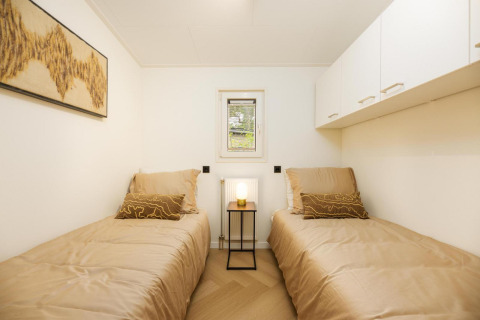 Habitación moderna de lodge con dos camas individuales, ropa de cama beige, arte y lámpara encendida.