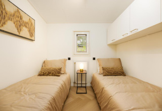 Habitación moderna de lodge con dos camas individuales, ropa de cama beige, arte y lámpara encendida.