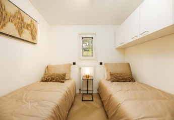 Moderne lodge-værelse med to enkelt senge, beige sengetøj, kunstværk og natbord med lampe.