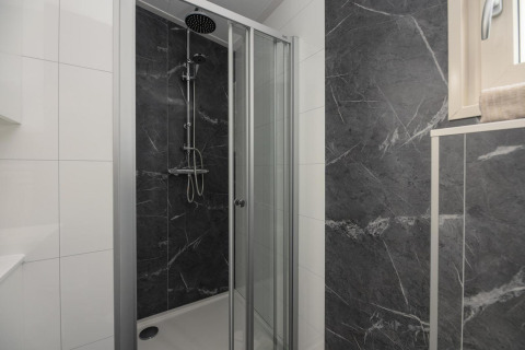 Ducha moderna con puertas de vidrio y azulejos oscuros en Loevestein Comfort, Veluwepark de Bosgraaf, Países Bajos.