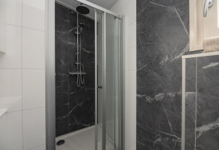 Ducha moderna con puertas de vidrio y azulejos oscuros en Loevestein Comfort, Veluwepark de Bosgraaf, Países Bajos.