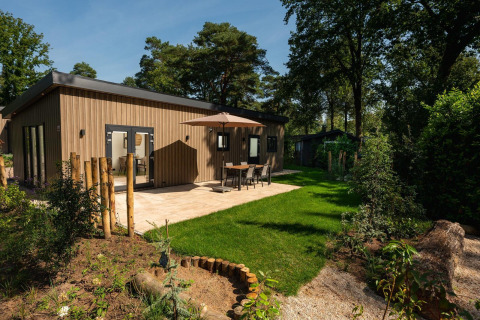Lodge Loevestein moderno con jacuzzi, terraza con mesa y paraguas, rodeado de bosque y jardín verde.