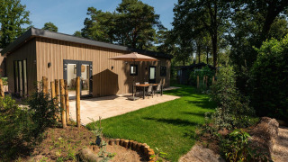 Modern Lodge Loevestein with hot tub, patio seating under umbrella, surrounded by green forest and garden.