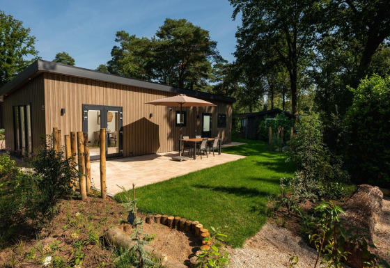 Lodge Loevestein moderno con jacuzzi, terraza con mesa y paraguas, rodeado de bosque y jardín verde.