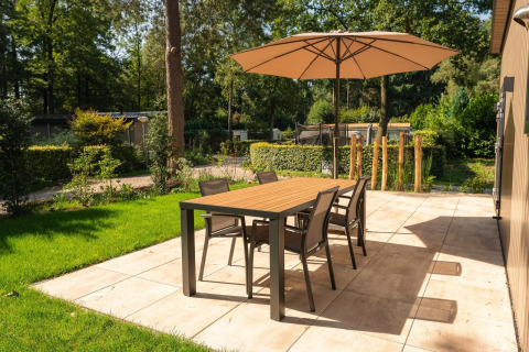Patio at Loevestein lodge with umbrella, dining table and four chairs at Veluwepark de Bosgraaf, Netherlands.