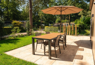 Terraza en la lodge Loevestein con sombrilla, mesa de comedor y cuatro sillas en Veluwepark de Bosgraaf, Países Bajos.