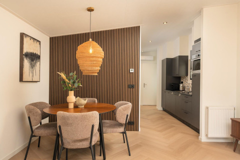 Comedor moderno en una cabaña, con mesa redonda, cuatro sillas, pared de madera y cocina integrada.
