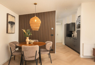 Comedor moderno en una cabaña, con mesa redonda, cuatro sillas, pared de madera y cocina integrada.