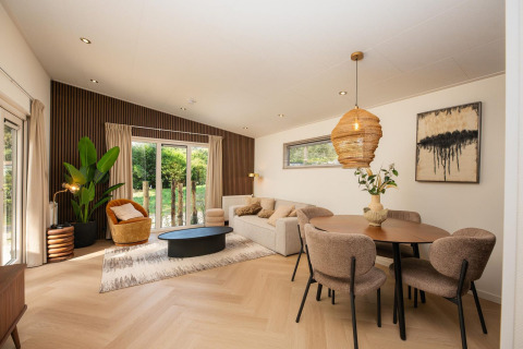 Sala de estar moderna en una cabaña con comedor, suelos de madera clara, grandes ventanales y decoración natural.