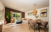Moderne lodge-stue med lyst trægulv, spiseområde, store vinduer og elegant indretning med naturlige elementer.