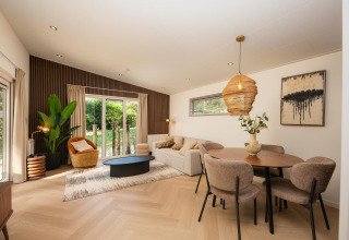 Sala de estar moderna en una cabaña con comedor, suelos de madera clara, grandes ventanales y decoración natural.