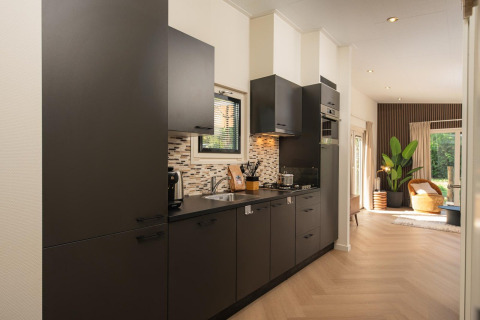 Cocina moderna en una cabaña con gabinetes oscuros, cocina de gas y vista hacia una sala iluminada.