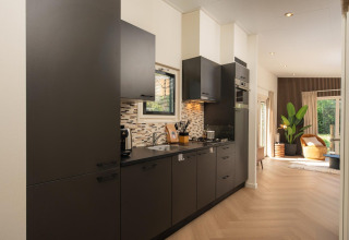 Cocina moderna en una cabaña con gabinetes oscuros, cocina de gas y vista hacia una sala iluminada.