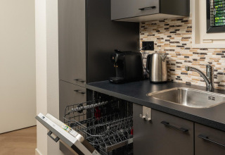 Zona de cocina moderna en lodge con lavavajillas abierto, cafetera, tetera eléctrica y pared de mosaico.