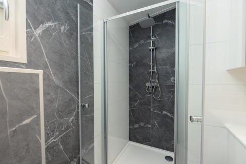 Cabina de ducha moderna en un alojamiento con puertas de cristal, ducha tipo lluvia y paredes de mármol oscuro.