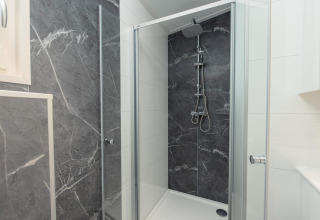 Cabina de ducha moderna en un alojamiento con puertas de cristal, ducha tipo lluvia y paredes de mármol oscuro.