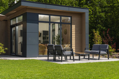 Modern lodge with large windows, outdoor seating area with garden furniture and green lawn in front.