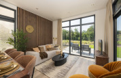 Moderne lodge-stue med store vinduer, neutrale farver, komfortabel sofa og udsigt til terrasse og natur.