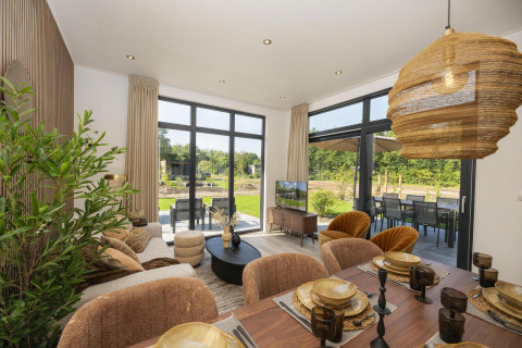 Helles Lodge-Wohnzimmer mit modernen Möbeln, großen Fenstern und Blick auf eine grüne Terrasse.
