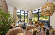 Lichte lodge woonkamer en eetruimte met moderne inrichting, grote ramen en uitzicht op de tuin.