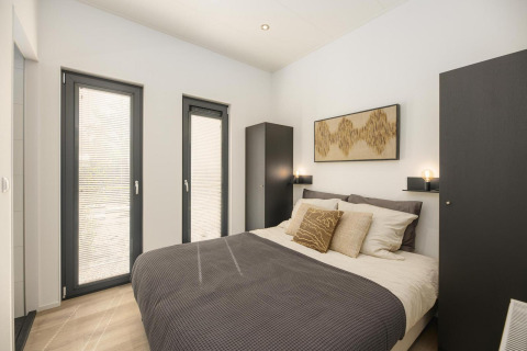 Modernes Schlafzimmer in einer Lodge mit Doppelbett, Kunstwerk, zwei Fenstern und Garderobe.