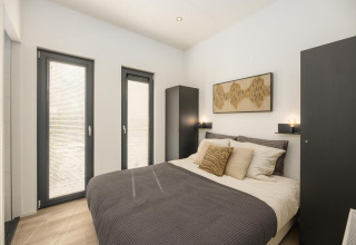 Modernes Schlafzimmer in einer Lodge mit Doppelbett, Kunstwerk, zwei Fenstern und Garderobe.