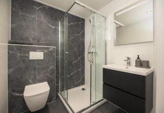 Baño moderno en una cabaña con ducha de vidrio, inodoro suspendido y mueble de lavabo negro con espejo.