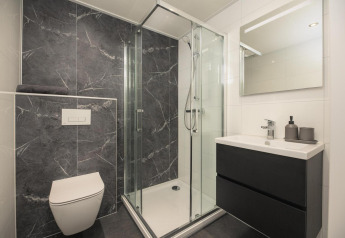 Moderne badeværelse på en lodge med glasbruser, vægmonteret toilet, sort vaskeskab og spejl.