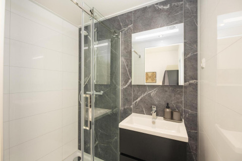 Baño moderno en un lodge con ducha de vidrio, espejo grande, mueble oscuro y paredes efecto mármol.