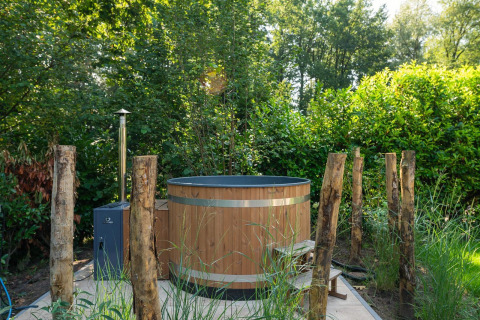 Bañera de hidromasaje exterior de madera rodeada de árboles y postes, en una lodge en plena naturaleza.