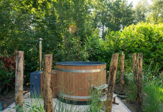 Bañera de hidromasaje exterior de madera rodeada de árboles y postes, en una lodge en plena naturaleza.
