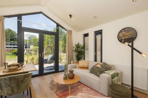 Bright living area inside Tiny Lodge with modern furniture, large windows, and outdoor view at Veluwepark de Bosgraaf.