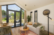 Lyst opholdsområde i Tiny Lodge med moderne indretning, store vinduer og udsigt til natur ved Veluwepark de Bosgraaf.