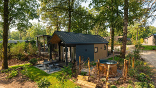 Moderna Tiny Loft lodge con vasca idromassaggio all’aperto tra alberi e natura rigogliosa per relax.