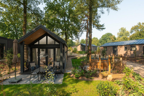 Pequeño lodge con jacuzzi exterior en Veluwepark de Bosgraaf, Países Bajos, rodeado de naturaleza y árboles.