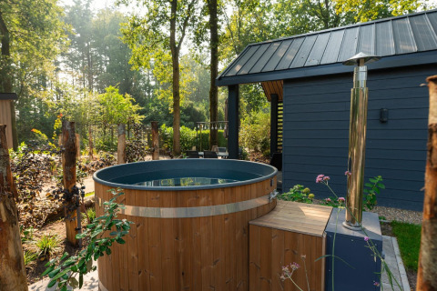 Bañera de hidromasaje de madera al aire libre junto a una cabaña moderna en Veluwepark de Bosgraaf, Países Bajos.